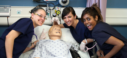 Nursing students striking a pose with a college patient dummy