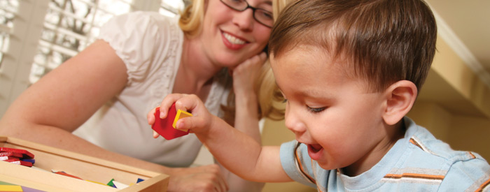 A toddler playing with blocks while a smiling woman watches him