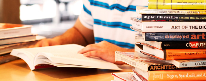 A student studying from a pile of books in a library